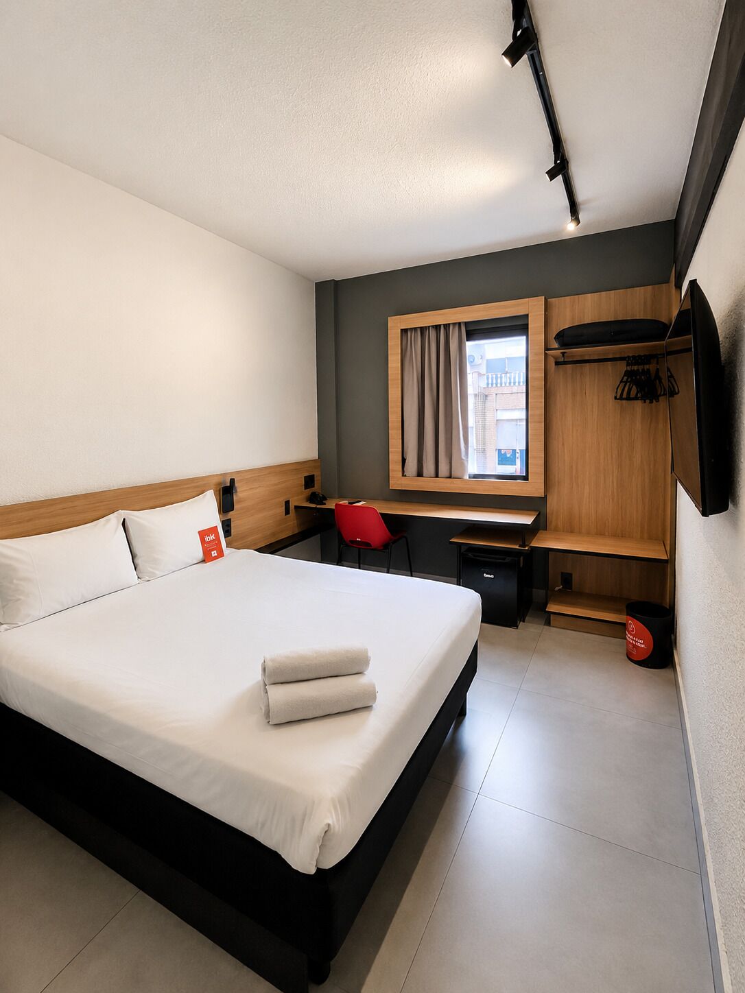 Quarto de hotel moderno com cama, escrivaninha, cadeira e armário.