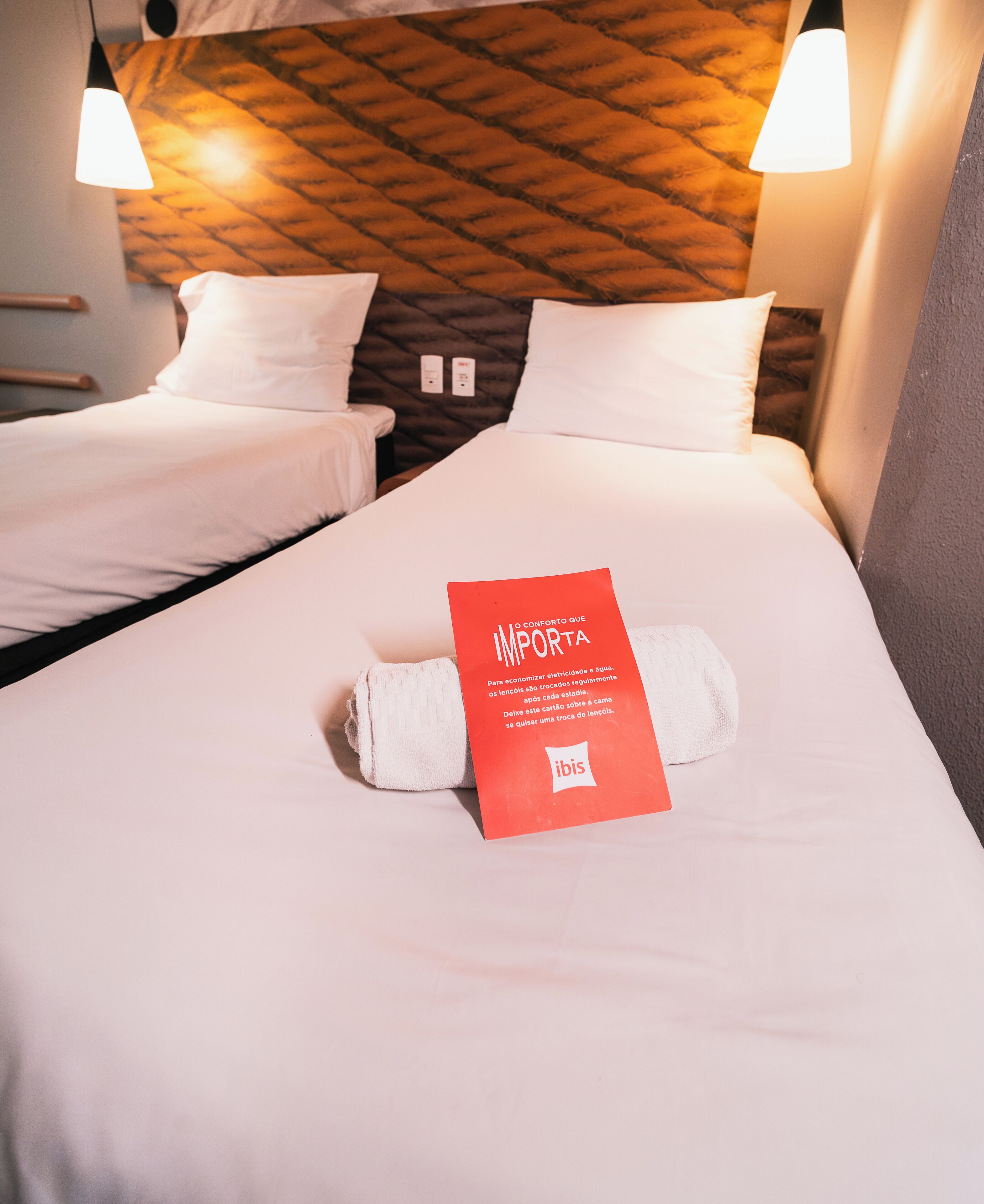 A hotel room with two beds, a red sign on the bed, and a wooden headboard.