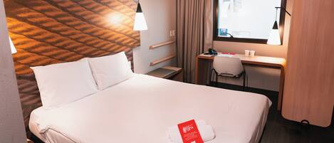 A hotel room with a bed, desk, and window.
