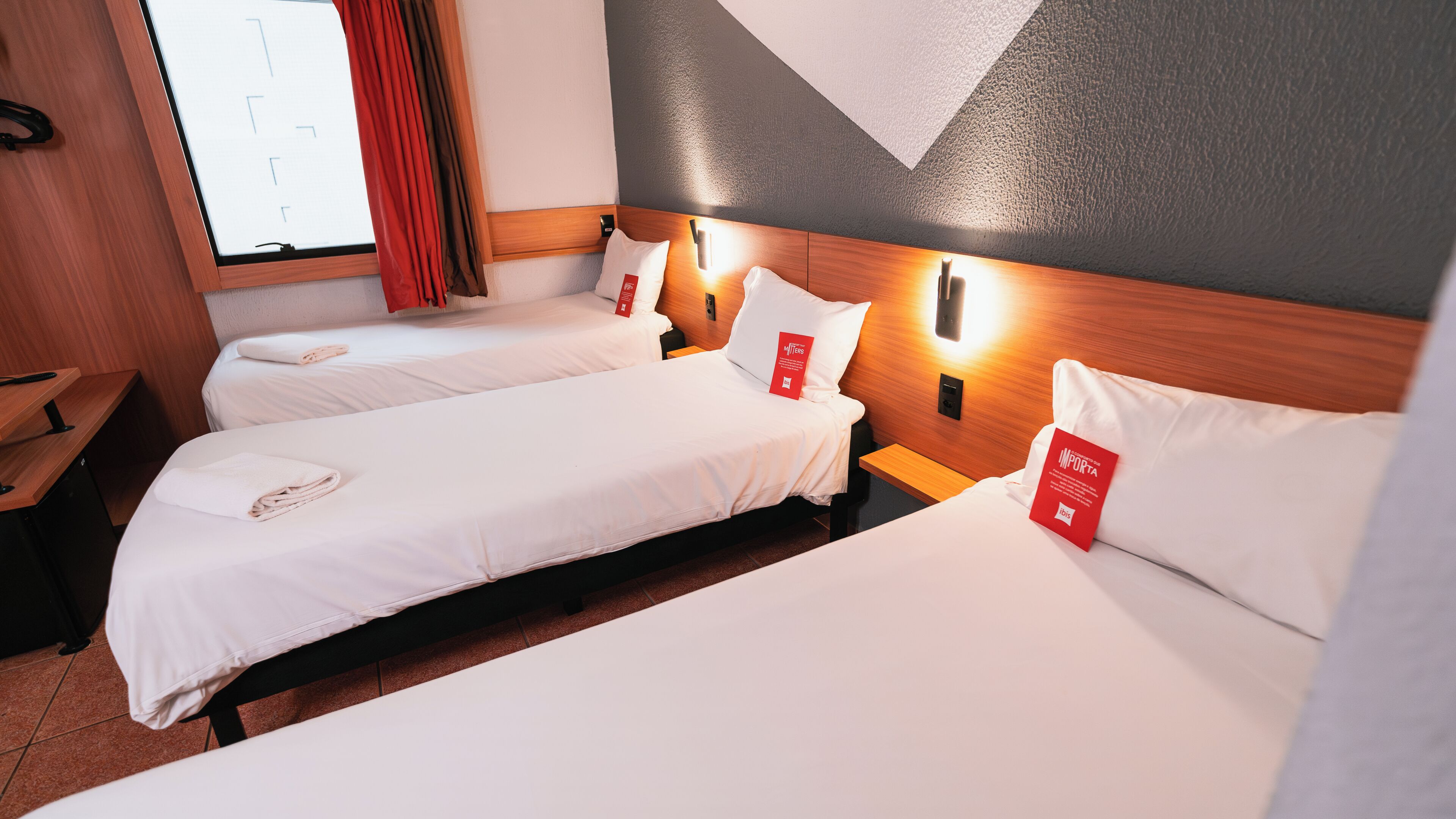 Quarto de hotel com duas camas, cabeceiras de madeira e uma janela com cortinas.