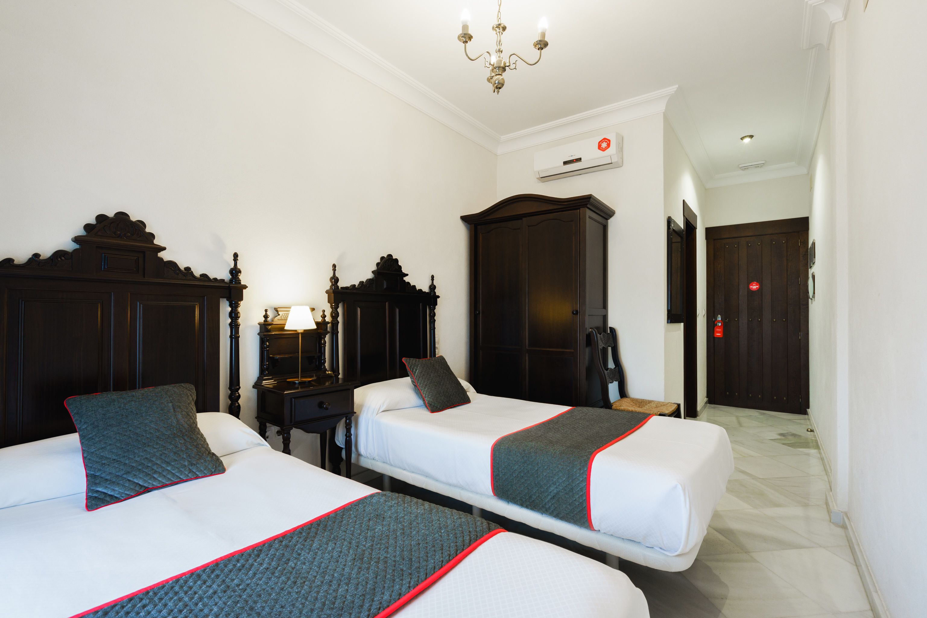 Habitación de hotel con dos camas, un armario, un escritorio con lámpara y un candelabro.