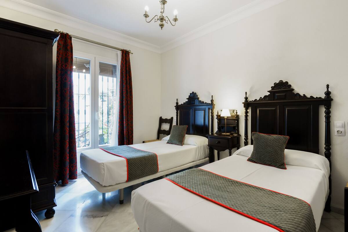 A hotel room with two beds, a piano, and a large window with curtains.