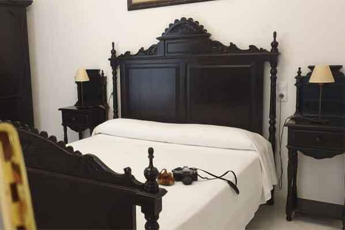 A bedroom with a dark wooden bed, two bedside tables with lamps, a clock, and a wardrobe.