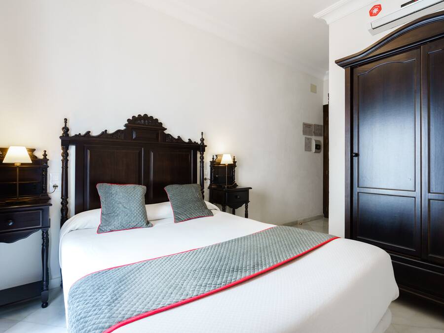 A neatly made bed with a quilted blanket, two bedside tables with lamps, and a dark wooden wardrobe.