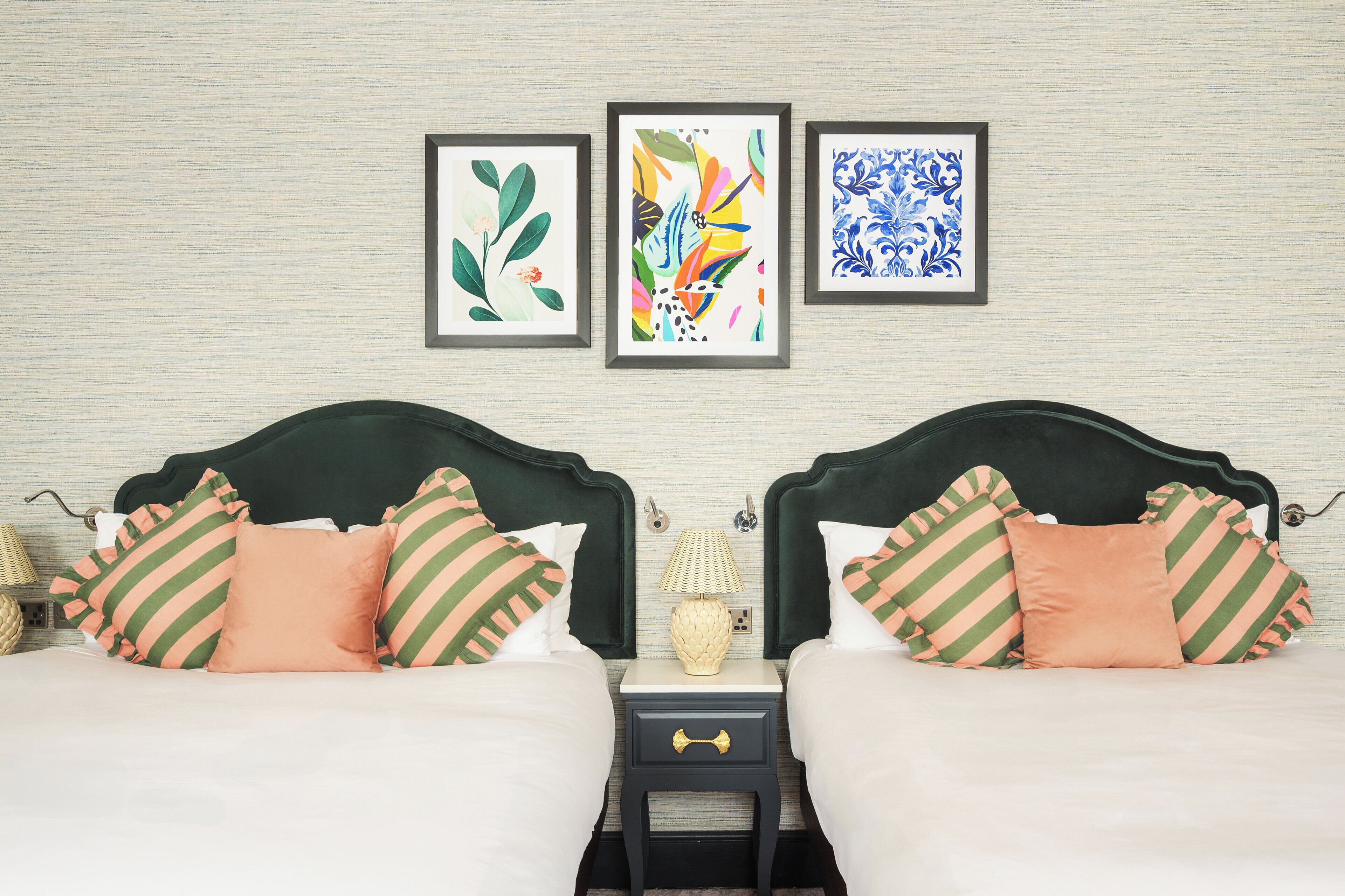 A double bed with striped pillows, a nightstand with a lamp, and three framed artworks on the wall.