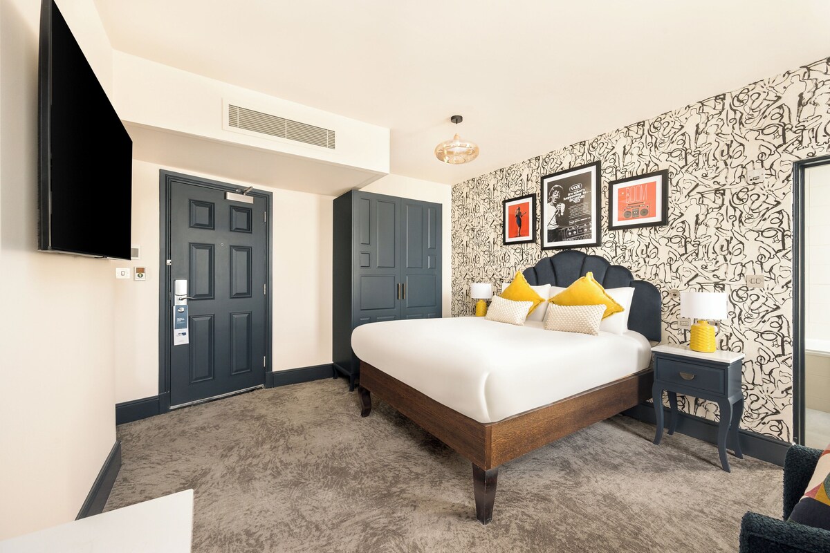 Une chambre à coucher avec un lit, une table de chevet, un téléviseur, une armoire et un mur décoré d’un motif.