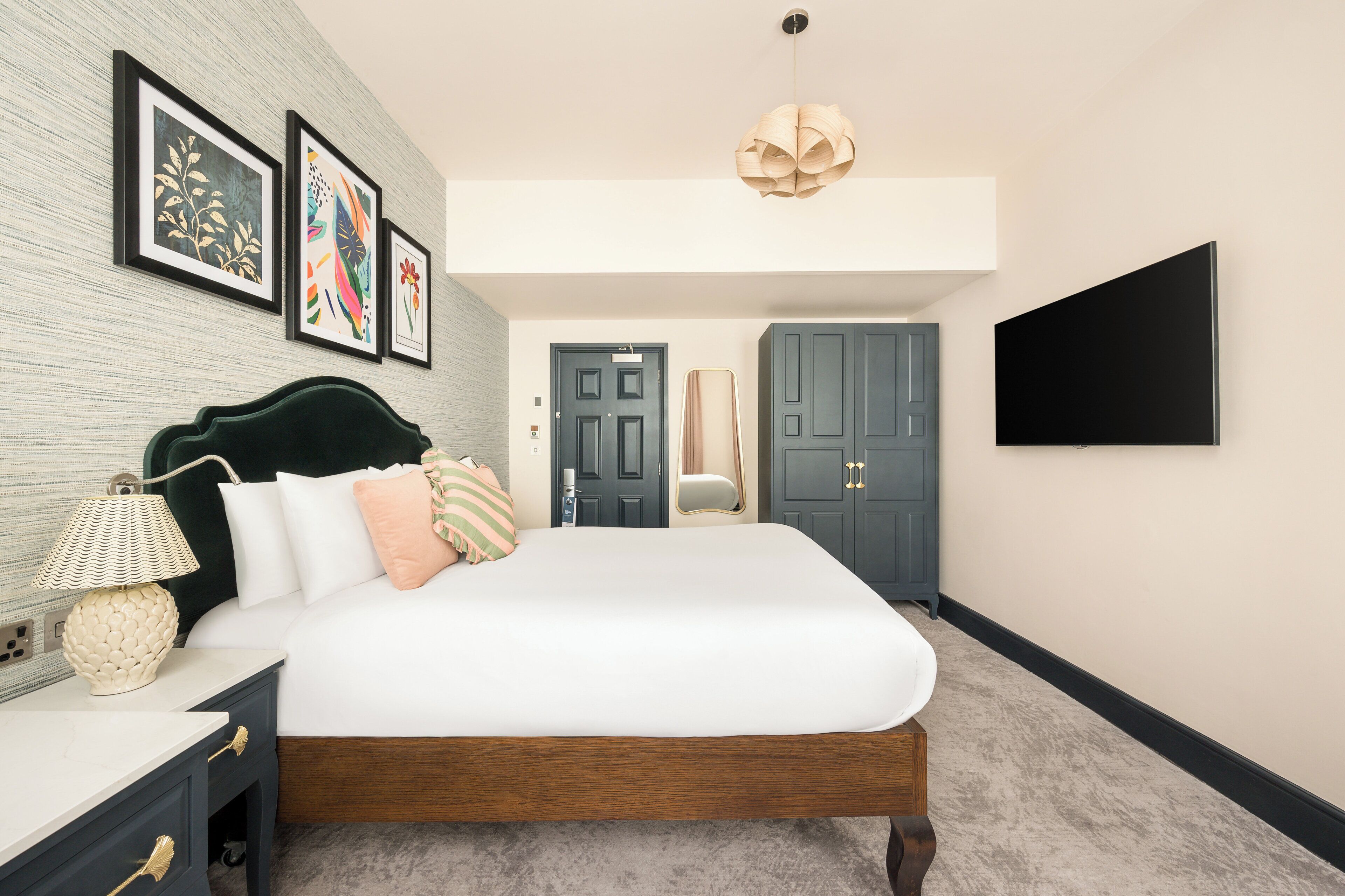 Un dormitorio con cama, mesita de noche, lámpara, decoración en la pared y televisor.