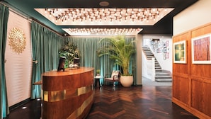 Un área de recepción con un mostrador de madera, una planta grande en maceta, una silla y una escalera que sube a un nivel superior.