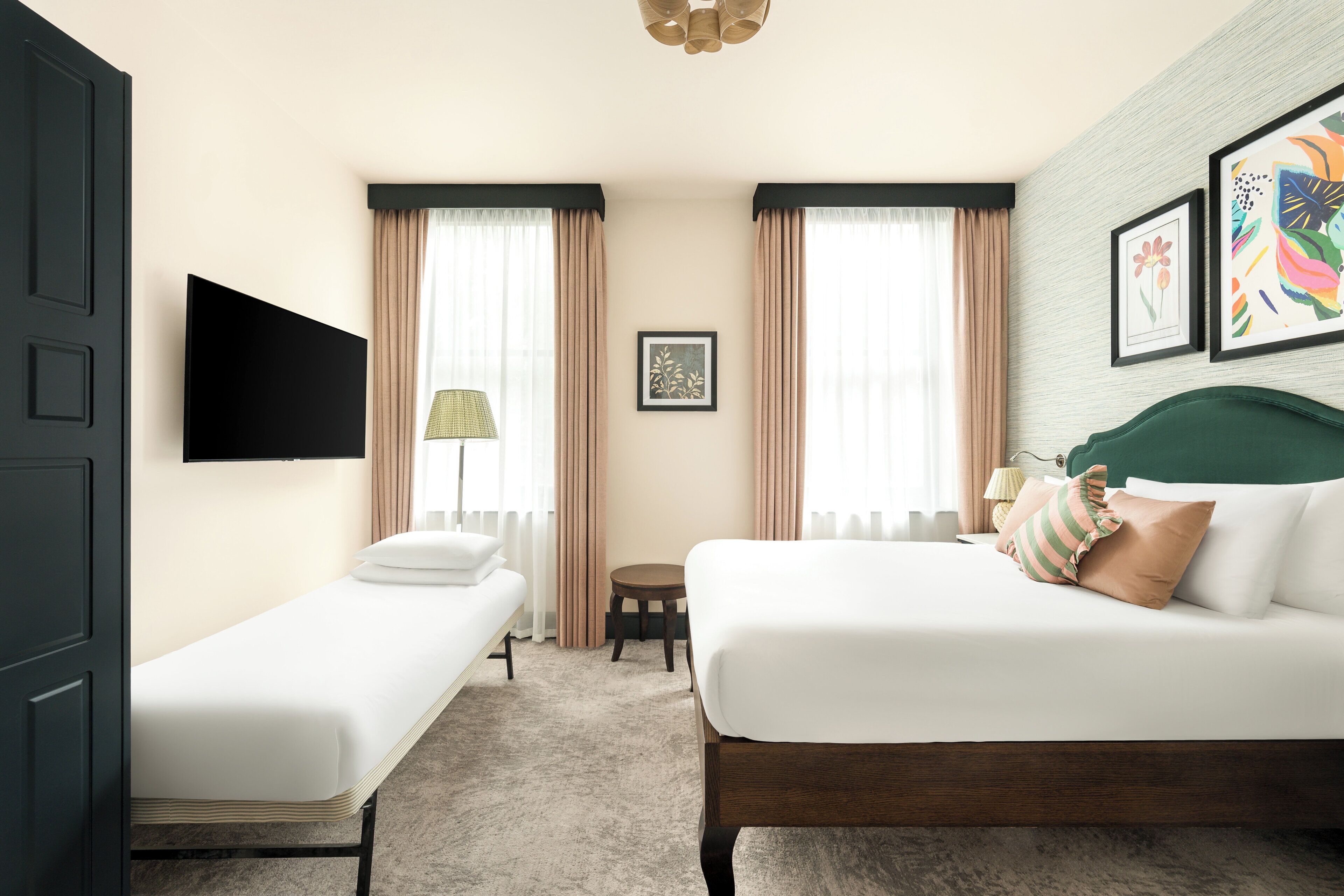 A hotel room with a bed, a smaller bed, a TV, a lamp, a picture on the wall, and a window with curtains.