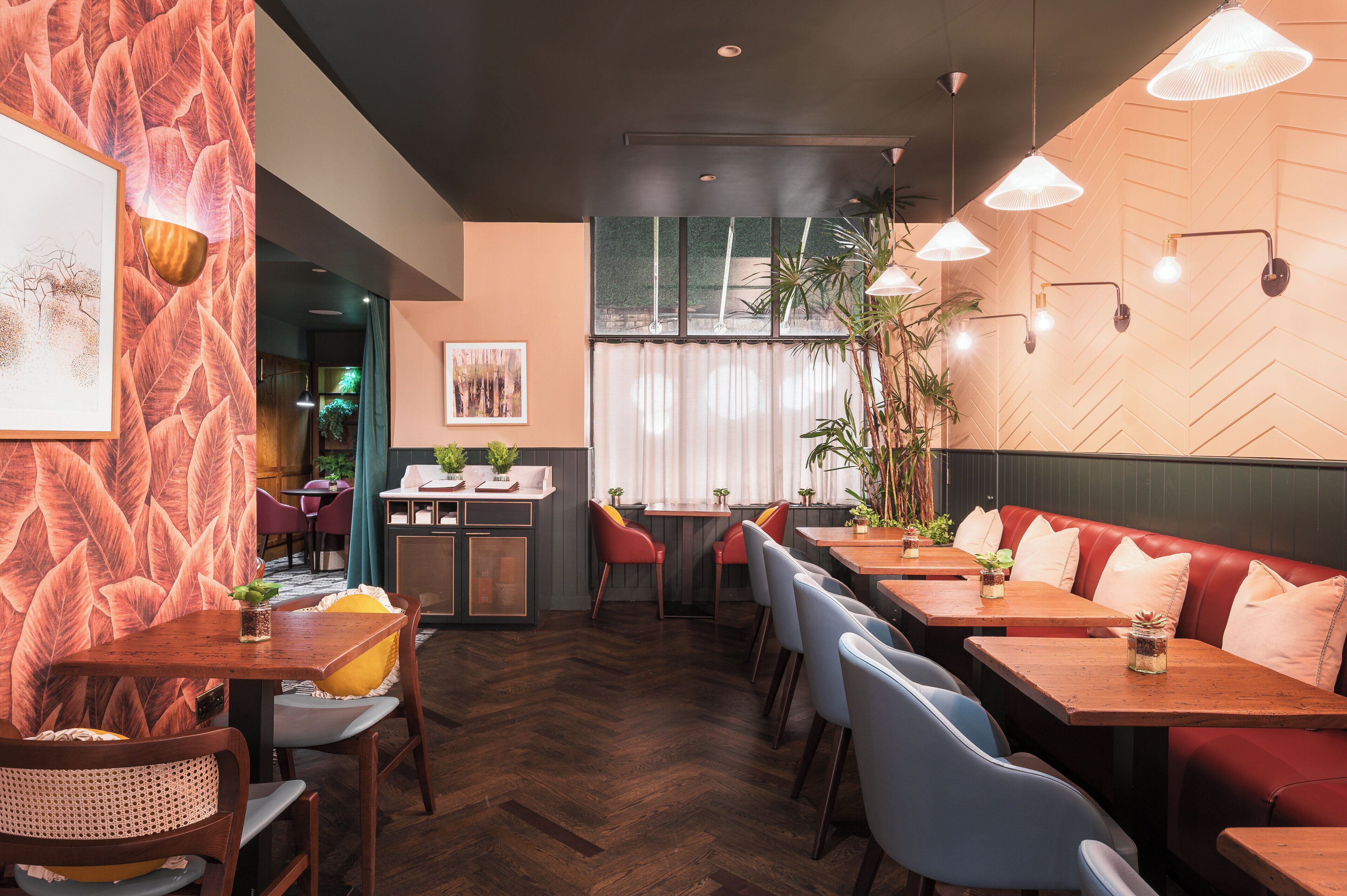 A restaurant interior with wooden tables, cushioned seating, pendant lighting, and a herringbone-patterned wall.