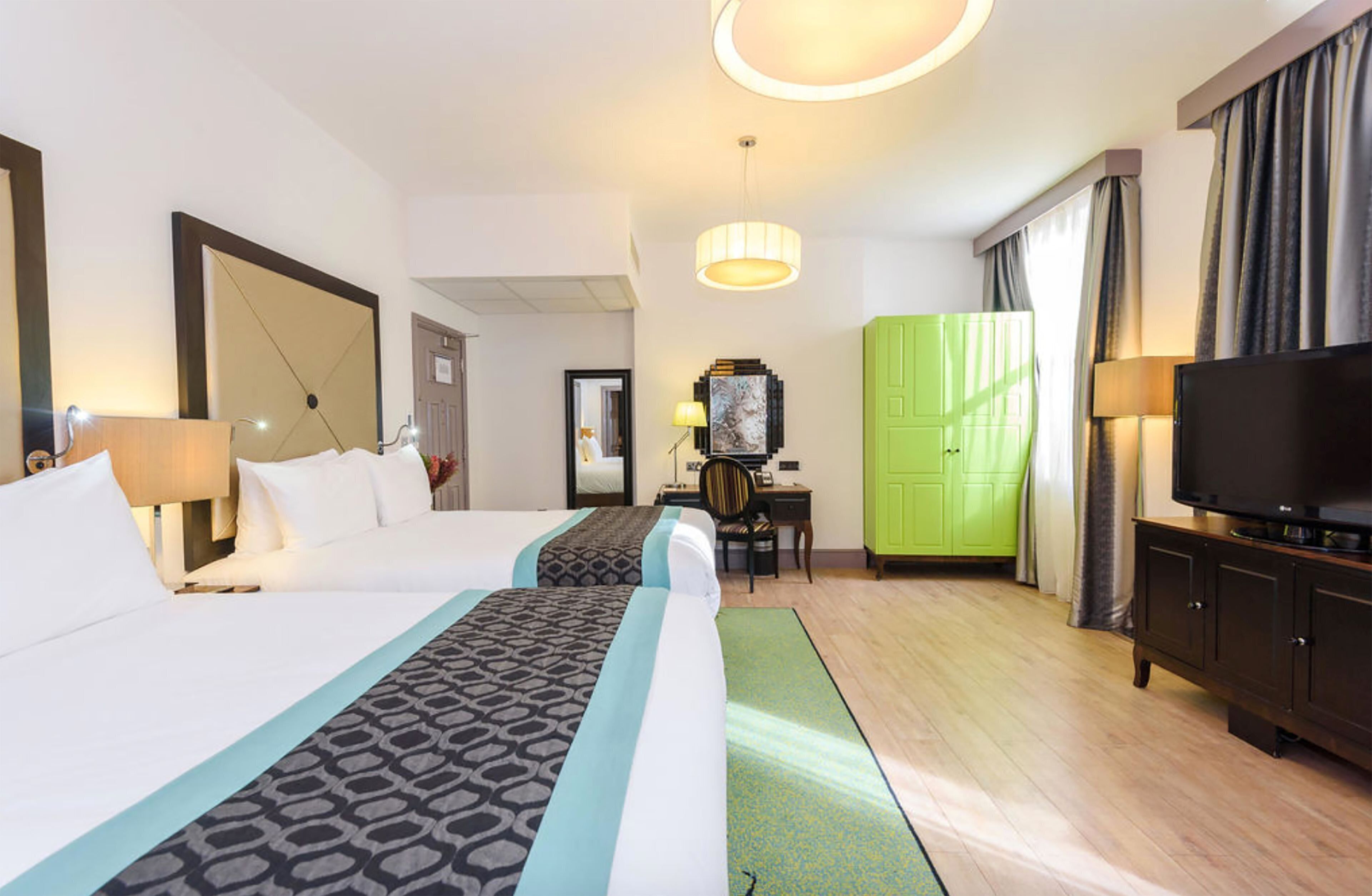 A hotel room with two beds, a desk, a television, and a green wardrobe.