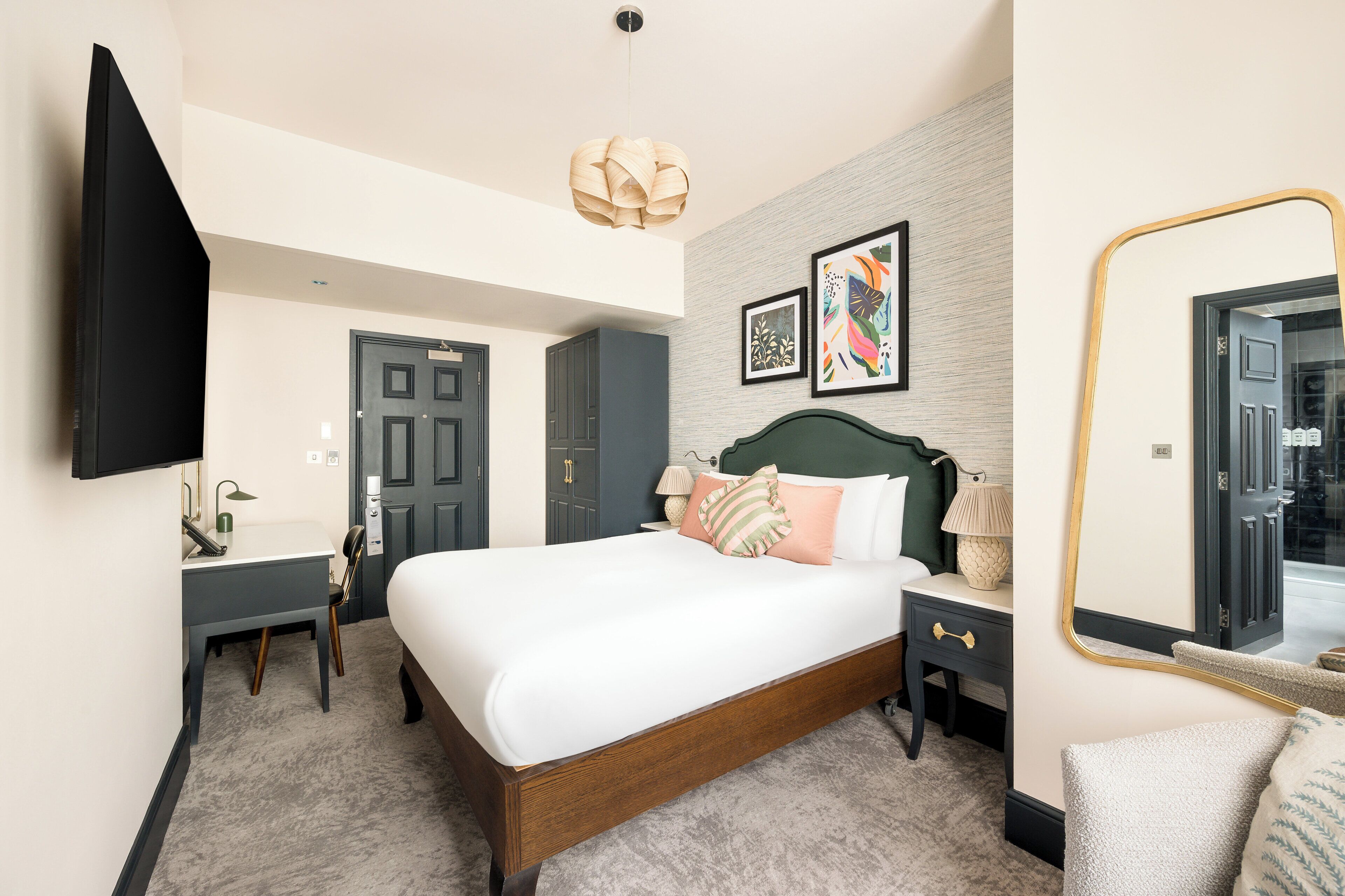 A hotel room with a bed, bedside table, lamp, and a flat-screen TV mounted on the wall.