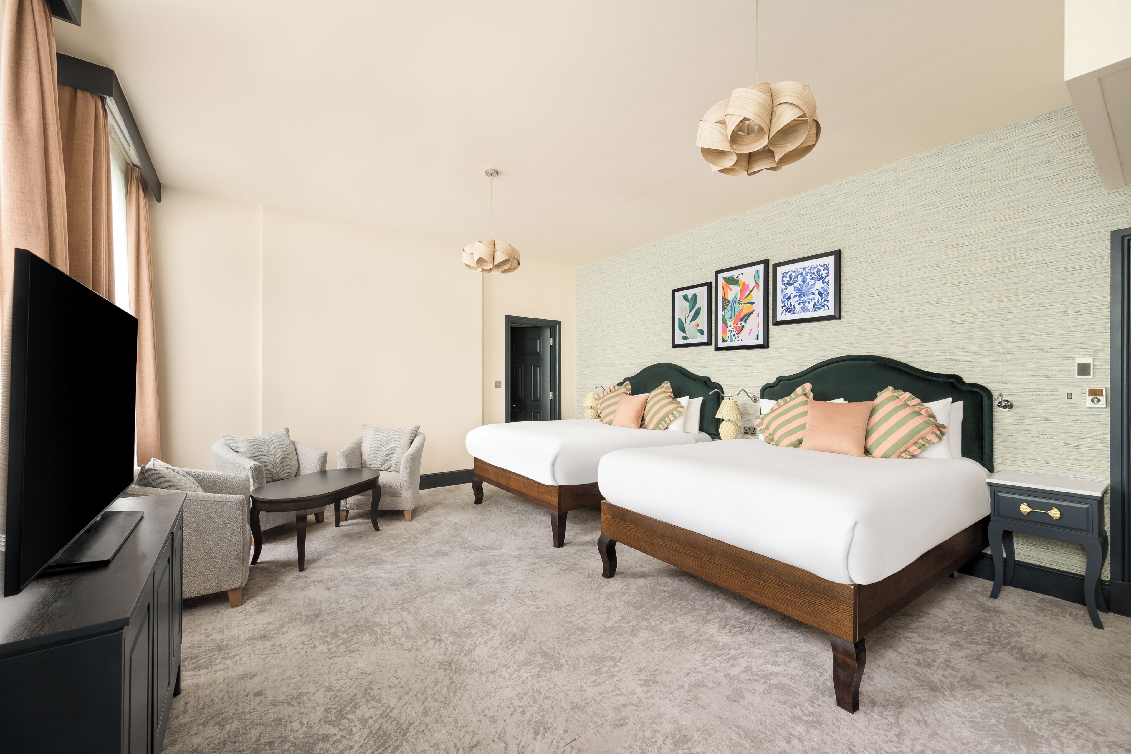 A hotel room with a TV, two beds, a sofa, a small table, and artwork on the wall.