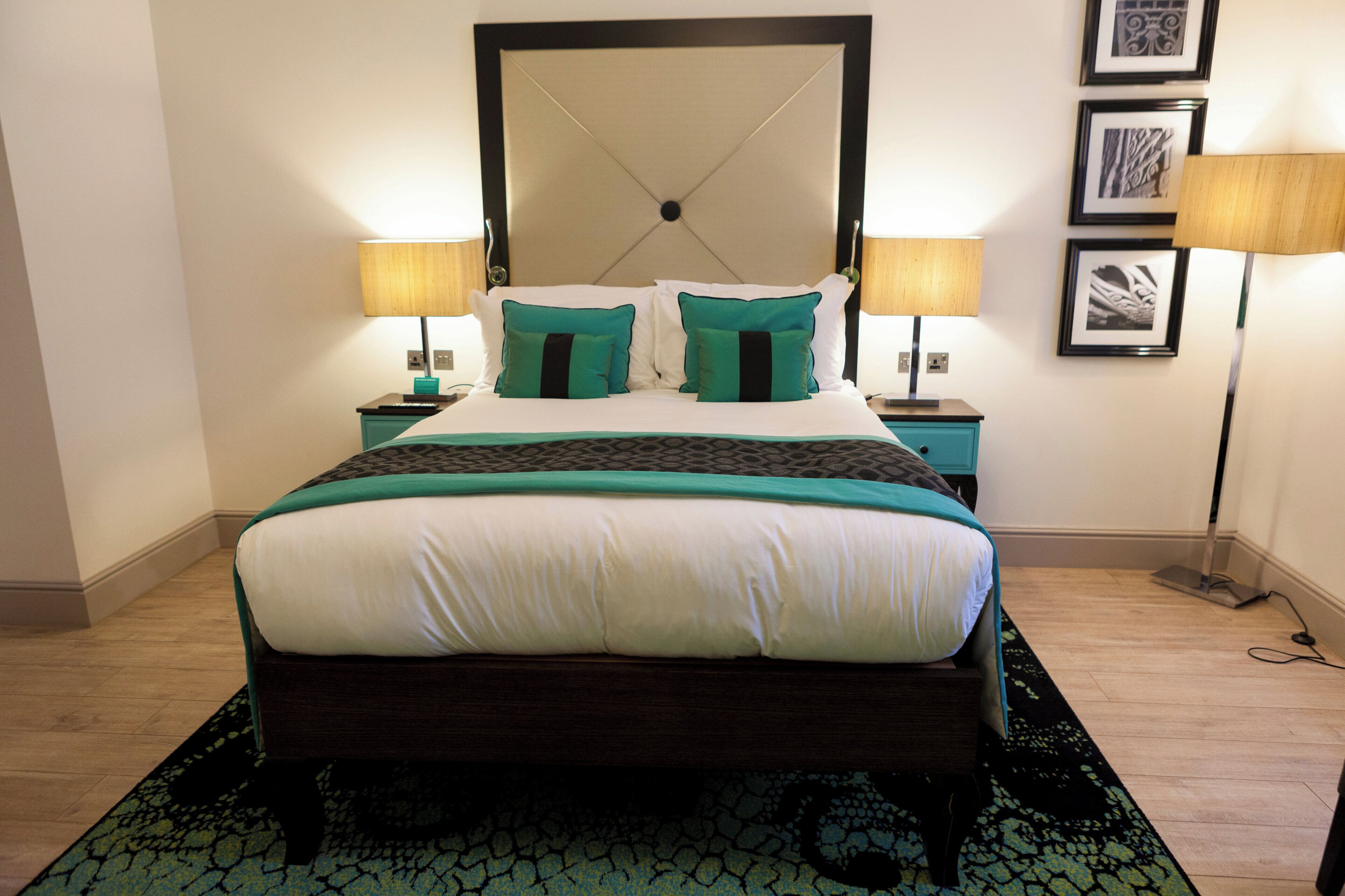 A neatly made bed with a dark headboard, two bedside tables with lamps, and a patterned rug on the floor.