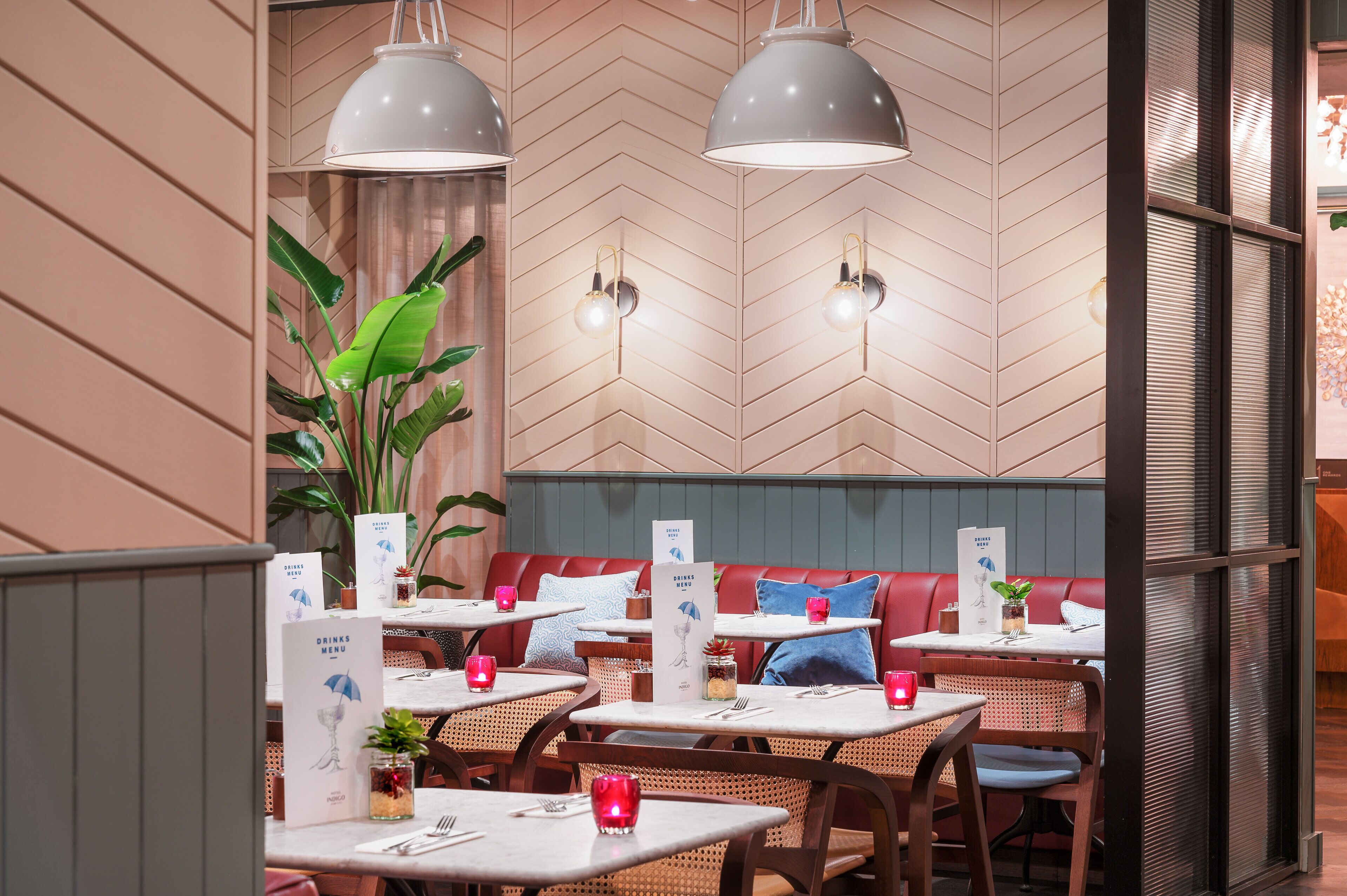 L’intérieur d’un restaurant présente des murs recouverts d’un motif en chevrons, des banquettes rouges et moelleuses, ainsi que des tables ornées de menus et de bougeoirs rouges.