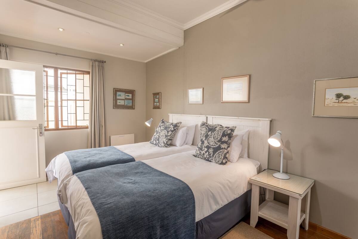 Una cama doble con dos mesitas de noche, una ventana con cortinas e imágenes enmarcadas en la pared.