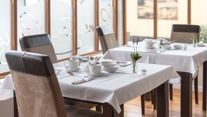 Comedor con mesas dispuestas para dos, manteles blancos y sillas con respaldo acolchado.