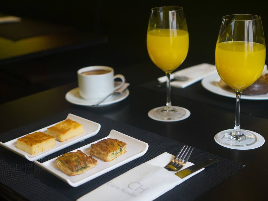 Una mesa con una taza de café, dos vasos de zumo de naranja y tres bollerías.