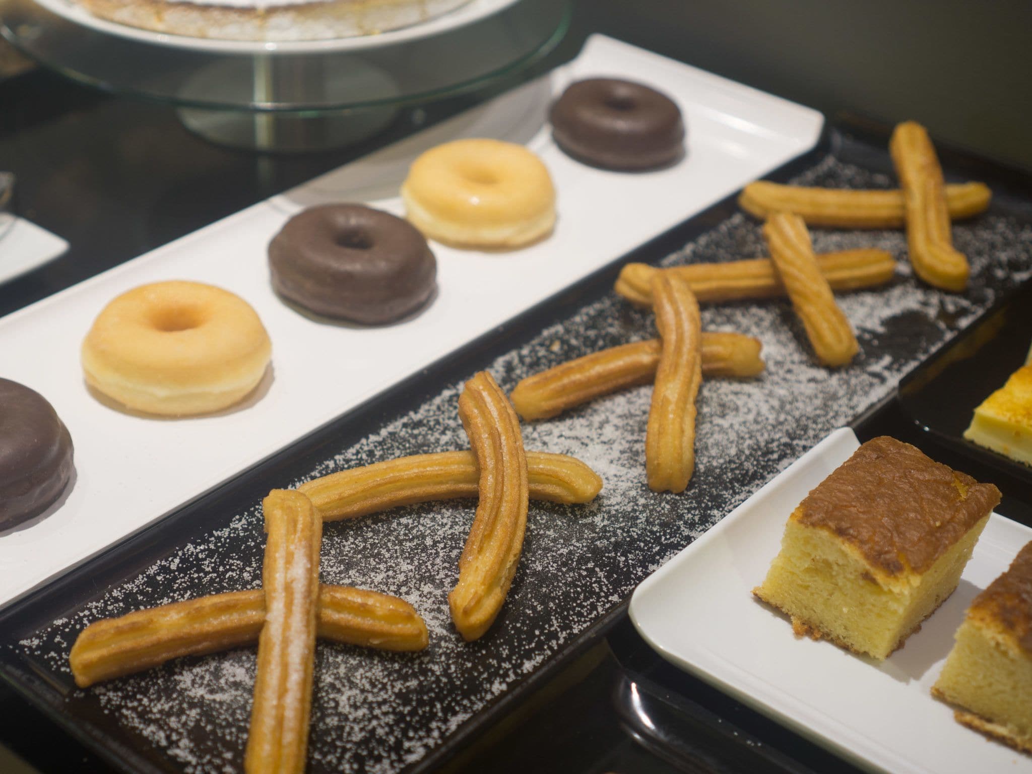 A tray of churros, doughnuts, and a slice of cake on a black plate.