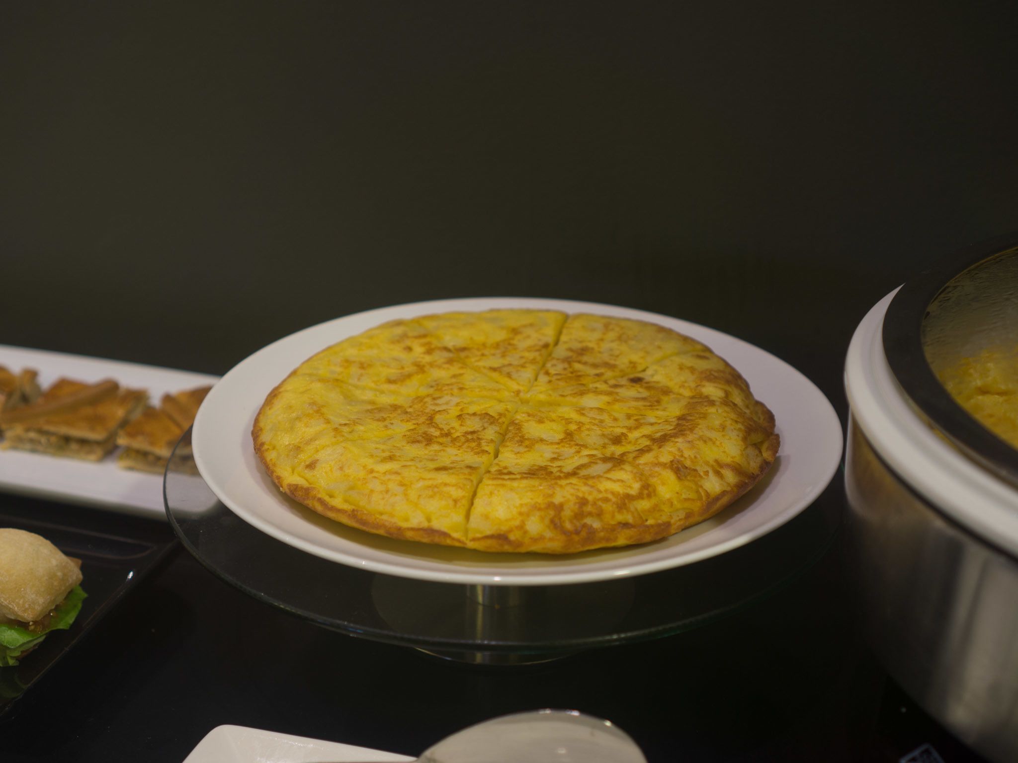 Un plato redondo y dorado, probablemente una especie de torta salada o tortilla, sobre un plato blanco, con fondo oscuro.