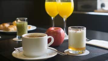Un desayuno con un croissant, jugo verde, una taza de café, una manzana y dos vasos de jugo de naranja.