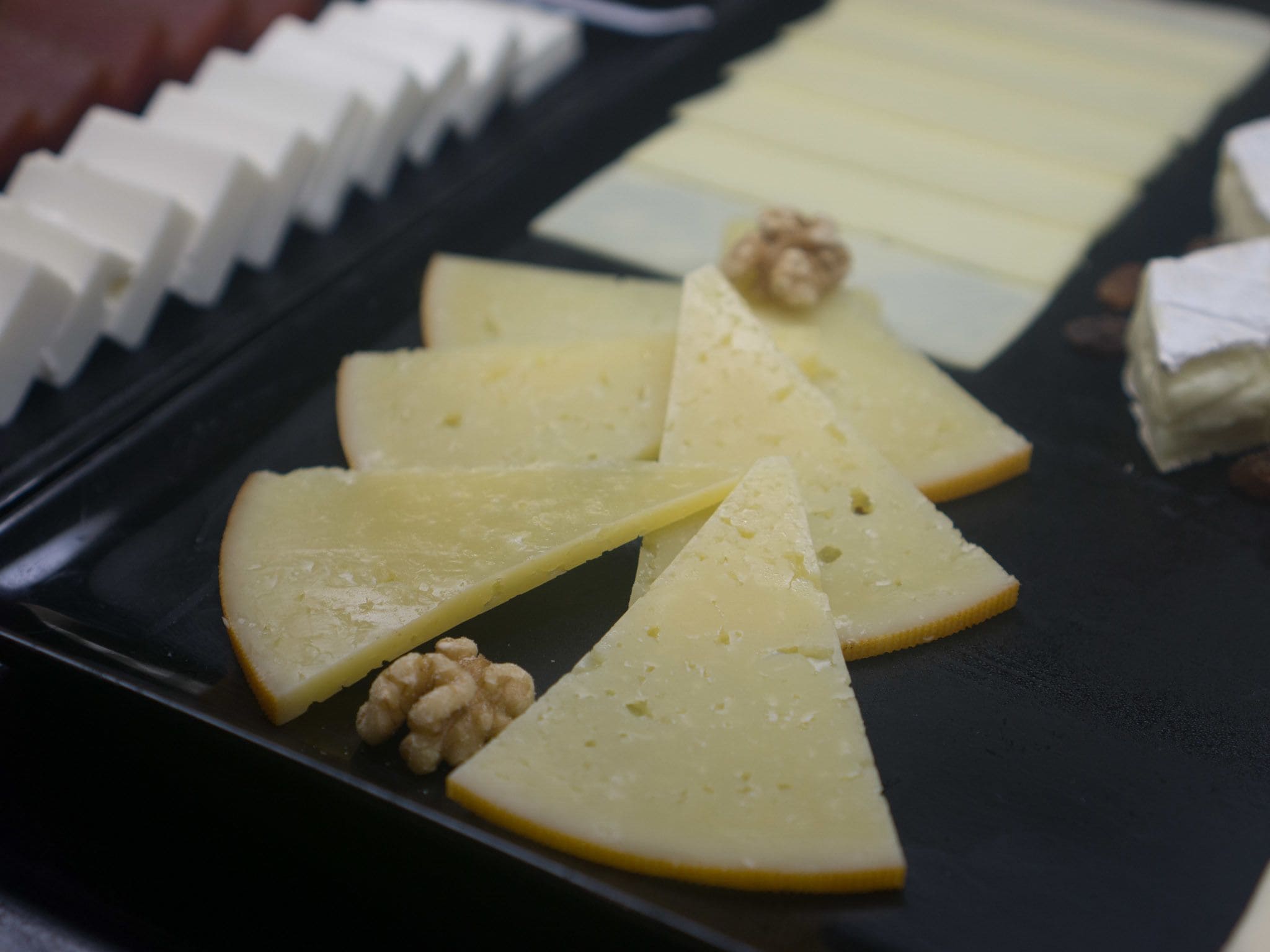 Variedad de rebanadas de queso y nueces sobre una bandeja negra.