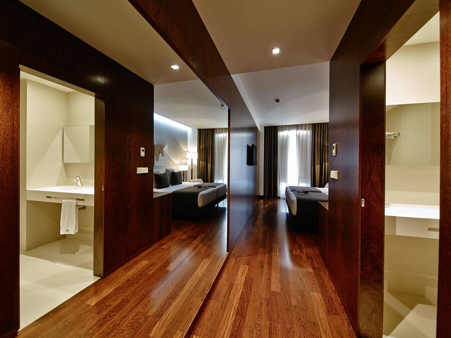 A modern hotel room with a wooden floor, a large bed, a separate bathroom, and a TV.
