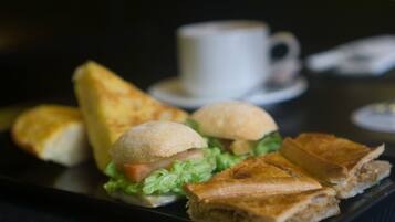 Un sándwich sobre un plato negro, con una taza de café al fondo.