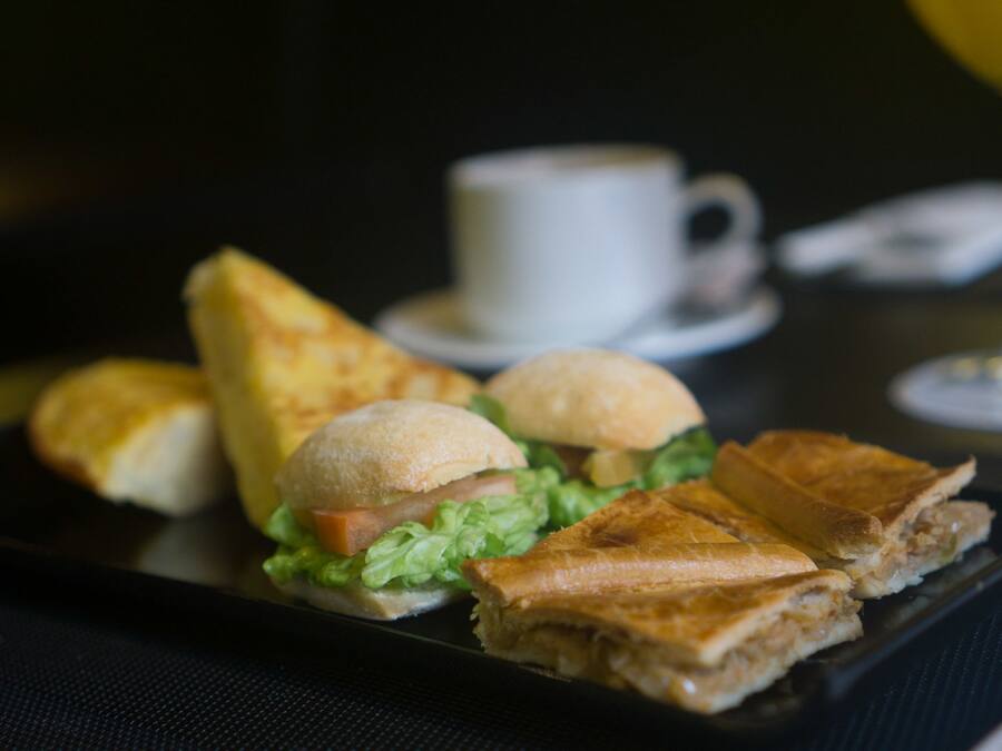 Un sándwich sobre un plato negro, con una taza de café al fondo.