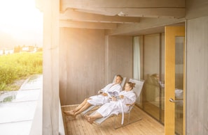 A couple relaxing in a sunlit room with a view of a garden and a bed visible through a glass door.
