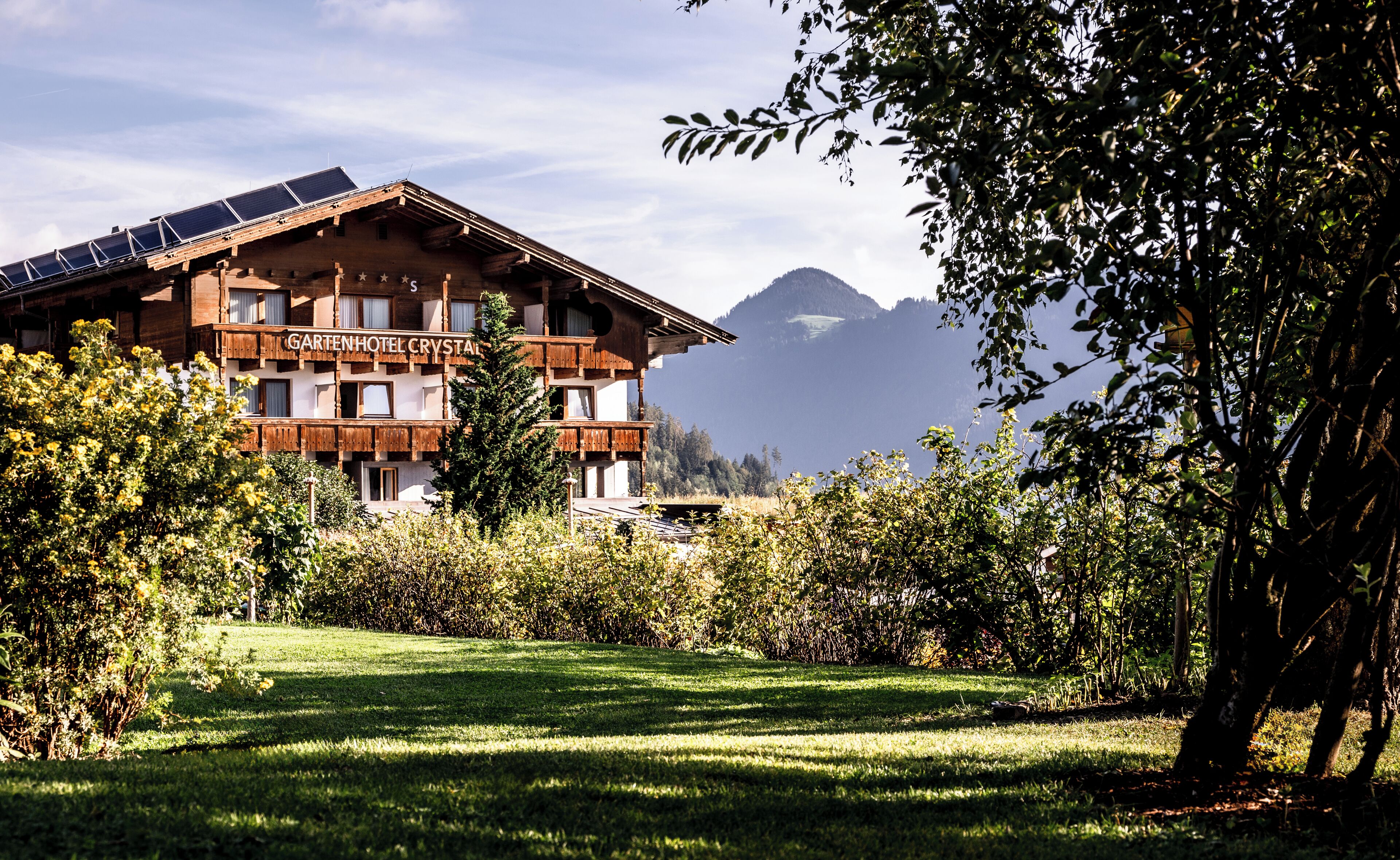 Ein Hotel mit Holzfassade, Solaranlage auf dem Dach und Bergblick im Hintergrund.