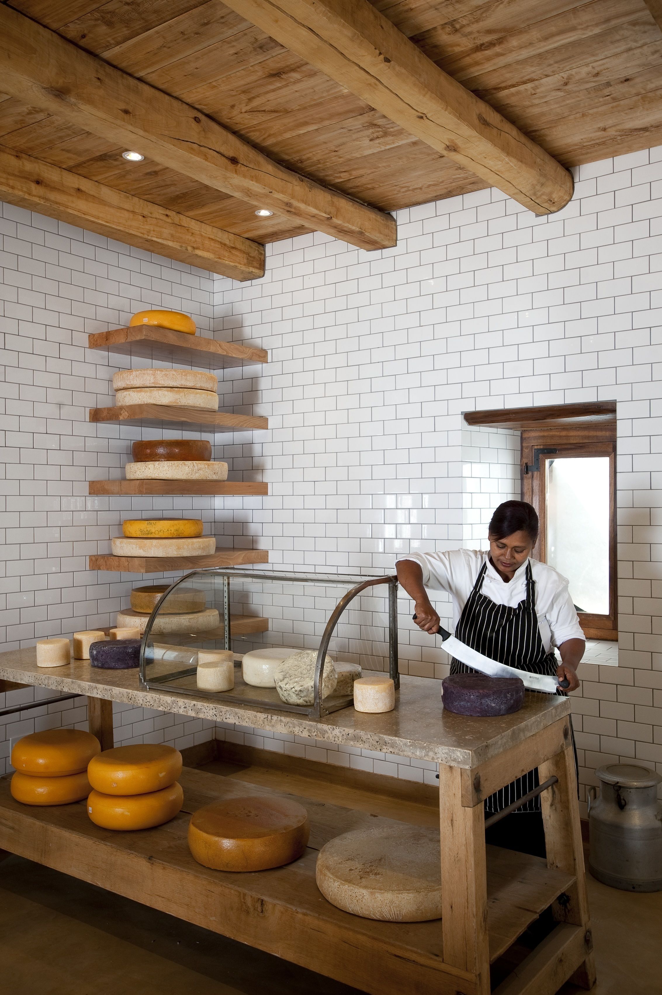 A cheese display with various types of cheese on wooden shelves and a cutting board.