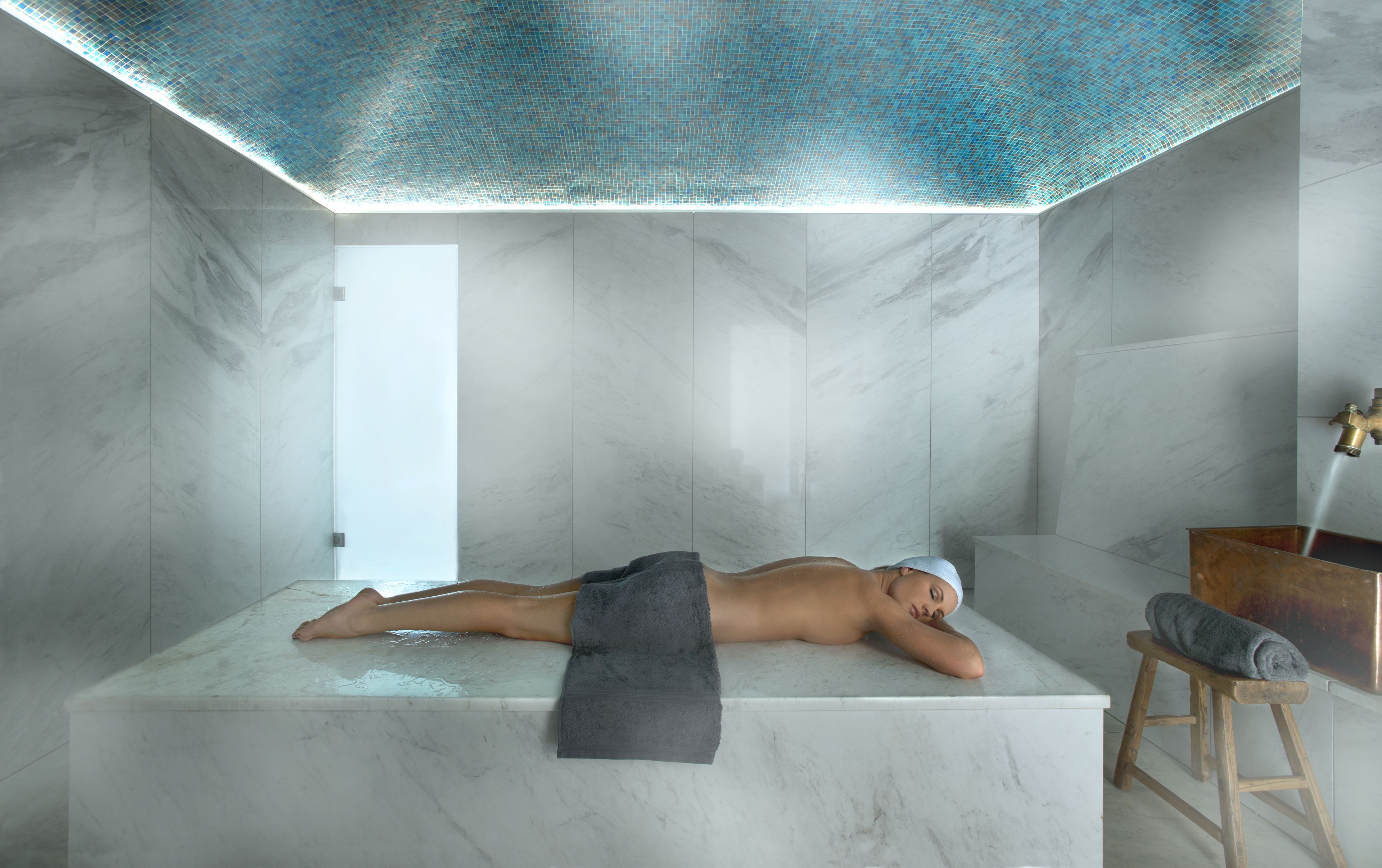 A spa room with a marble bathtub, a wooden stool, and a towel.