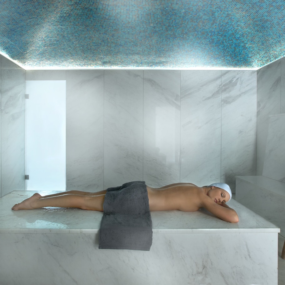A spa room with a marble bathtub, a wooden stool, and a towel.