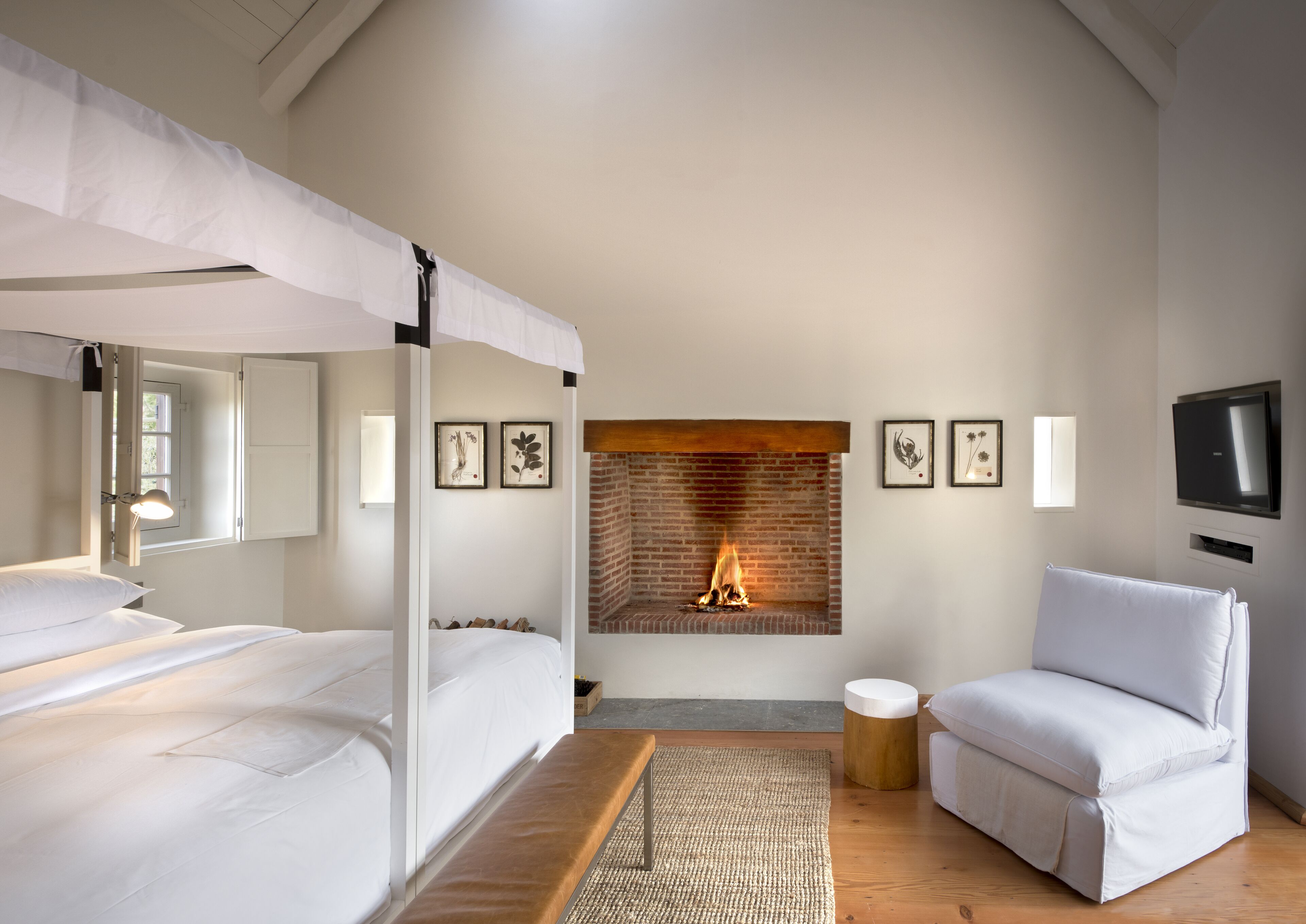 Une chambre avec une cheminée en briques, un lit à baldaquin, un canapé et un téléviseur fixé au mur.