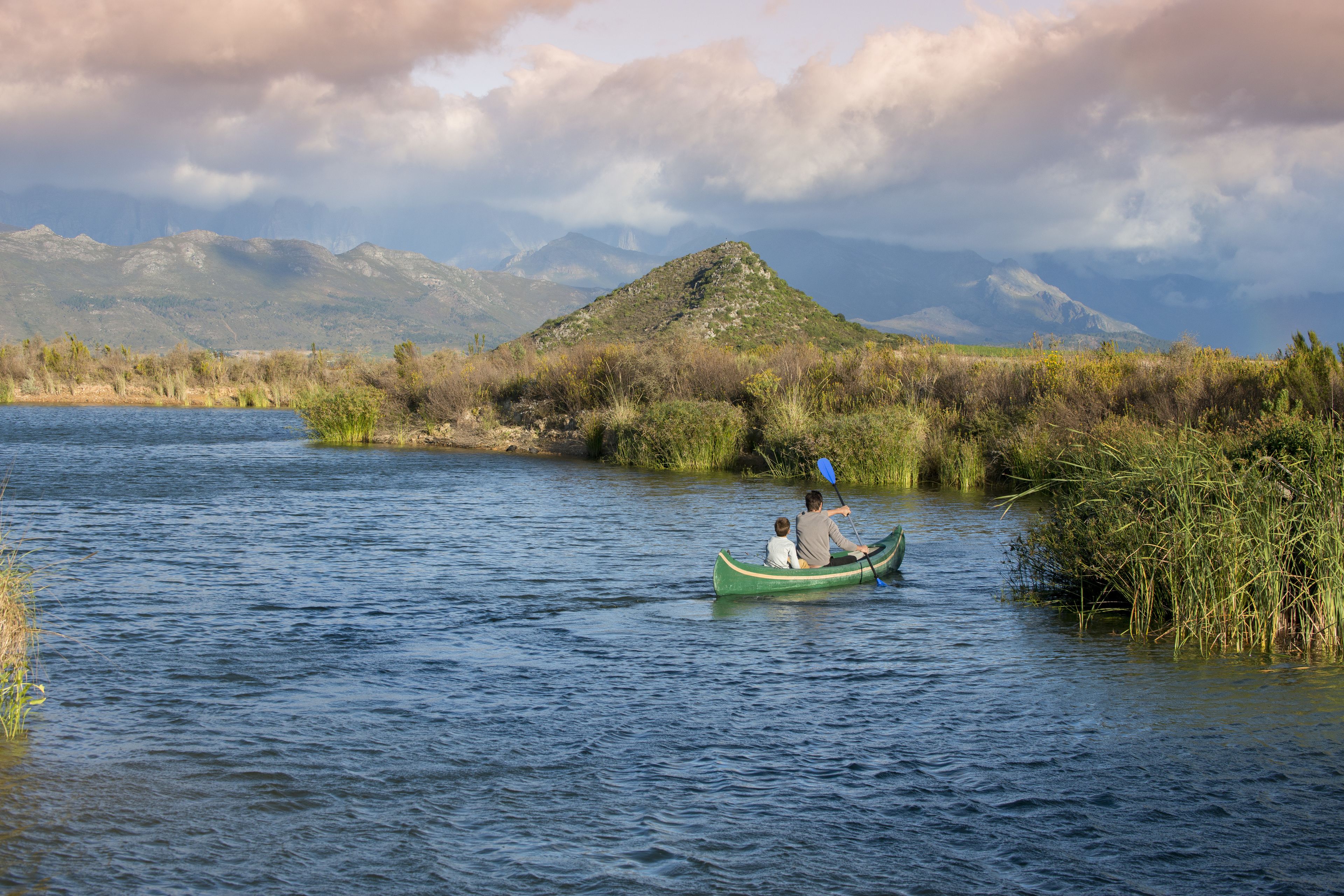 A green canoe on a calm river with mountains in the background.