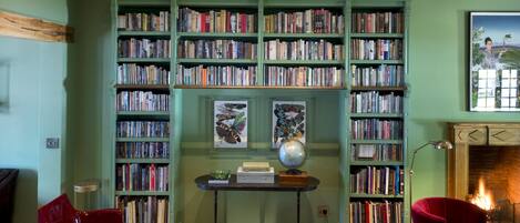 A room with a green sofa, red chairs, a fireplace, and bookshelves filled with books.