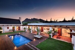 Una casa moderna con piscina, mobiliario exterior y vistas a montañas.