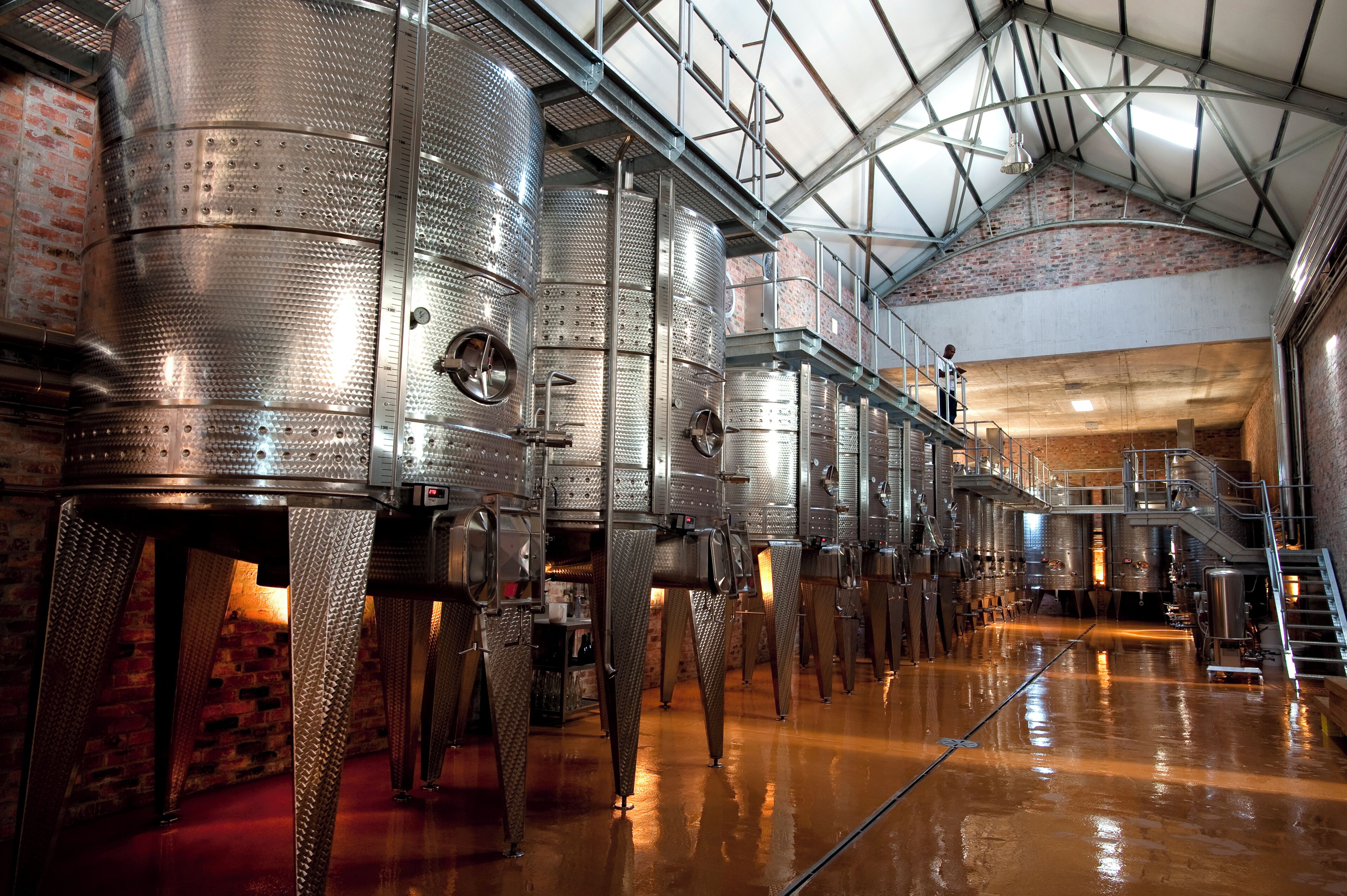 A large industrial space with stainless steel tanks, brick walls, and a high ceiling with metal beams.