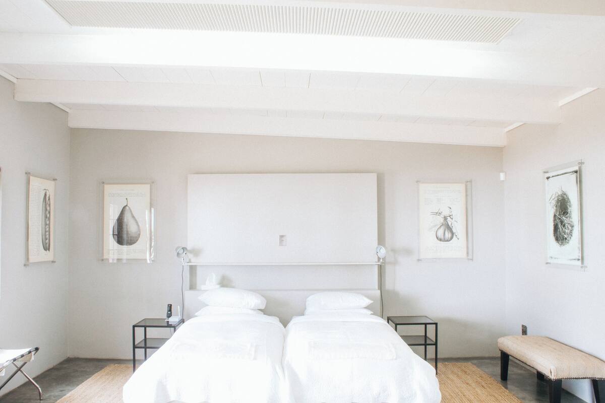 A minimalist bedroom with a large bed, bedside tables, a bench, and framed botanical prints on the walls.