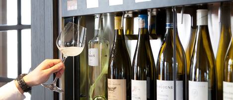 A hand holding a wine glass, with various wine bottles in a display case.