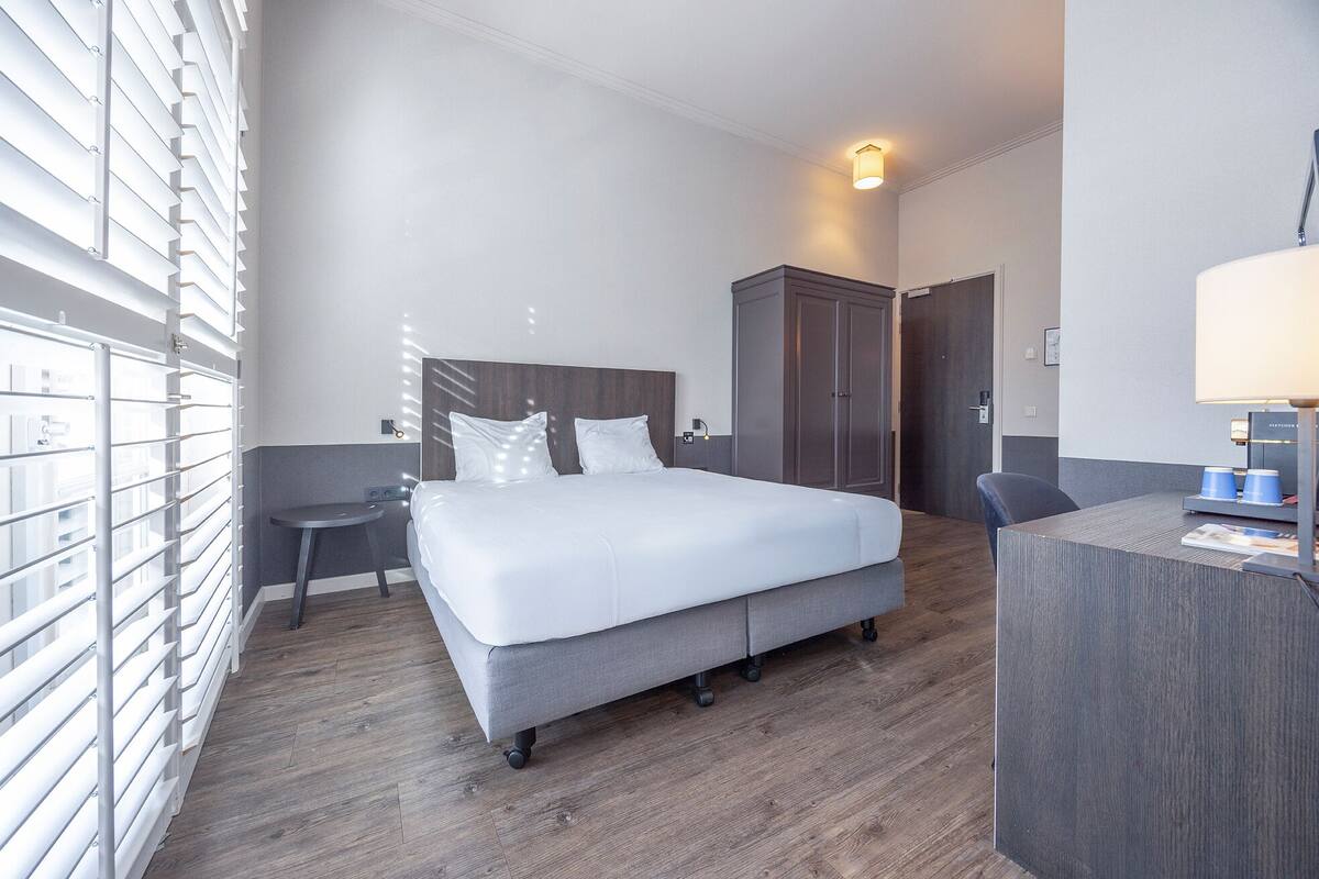 A hotel room with a large bed, a desk, and a wardrobe.