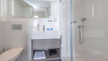 Un baño moderno con cabina de ducha de vidrio, un lavabo blanco con espejo superior y un inodoro a la izquierda.