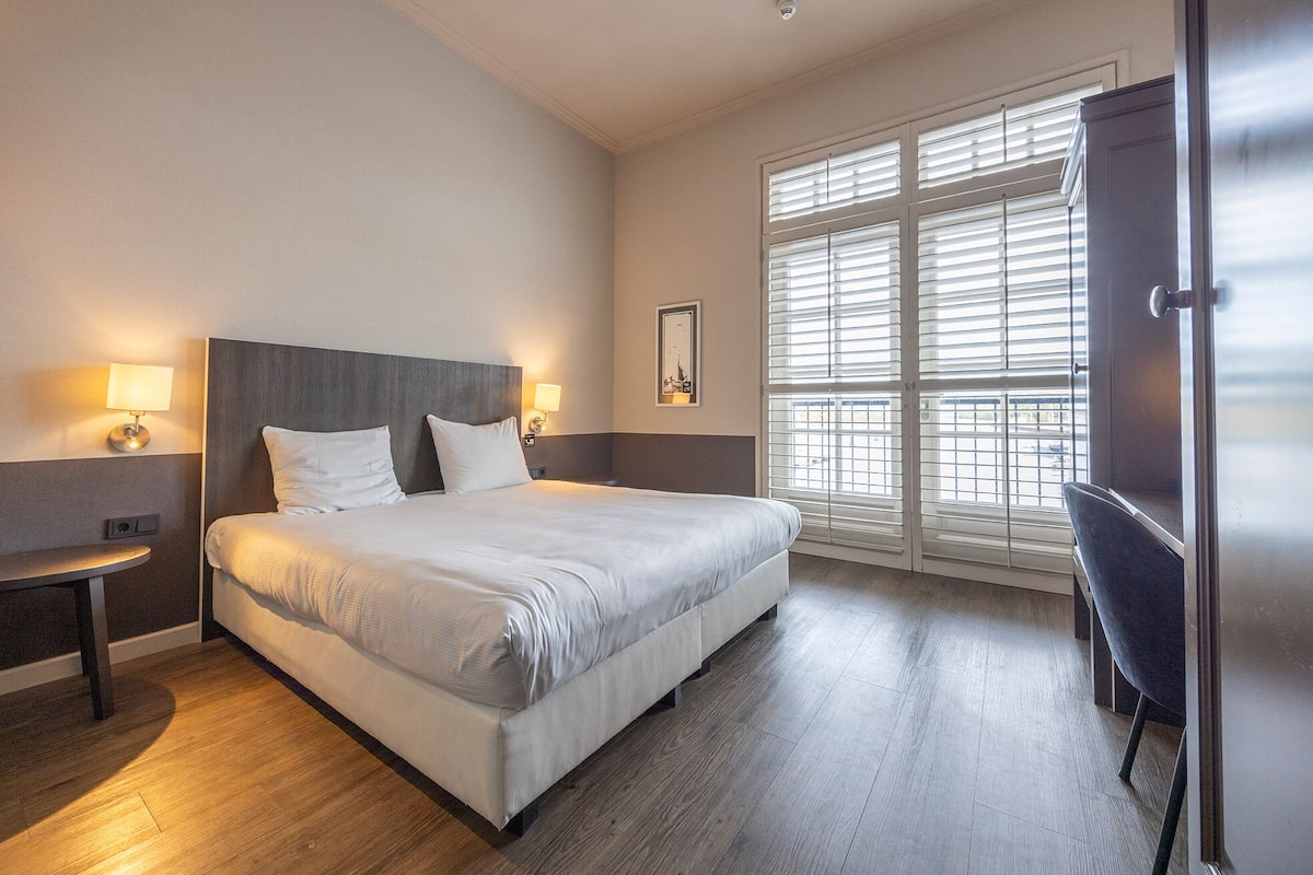 A hotel room with a large bed, bedside lamps, a desk, and a view through the window.