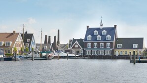 A waterfront with traditional buildings, a dock with boats, and a church steeple. - Fletcher Nautisch Kwartier (Huizen)
