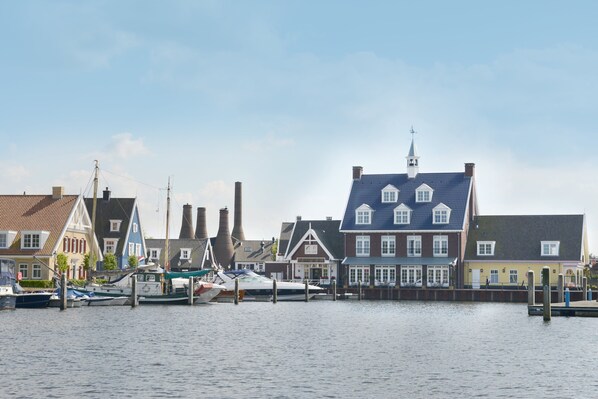 A waterfront with traditional buildings, a dock with boats, and a church steeple. - Fletcher Nautisch Kwartier (Huizen)