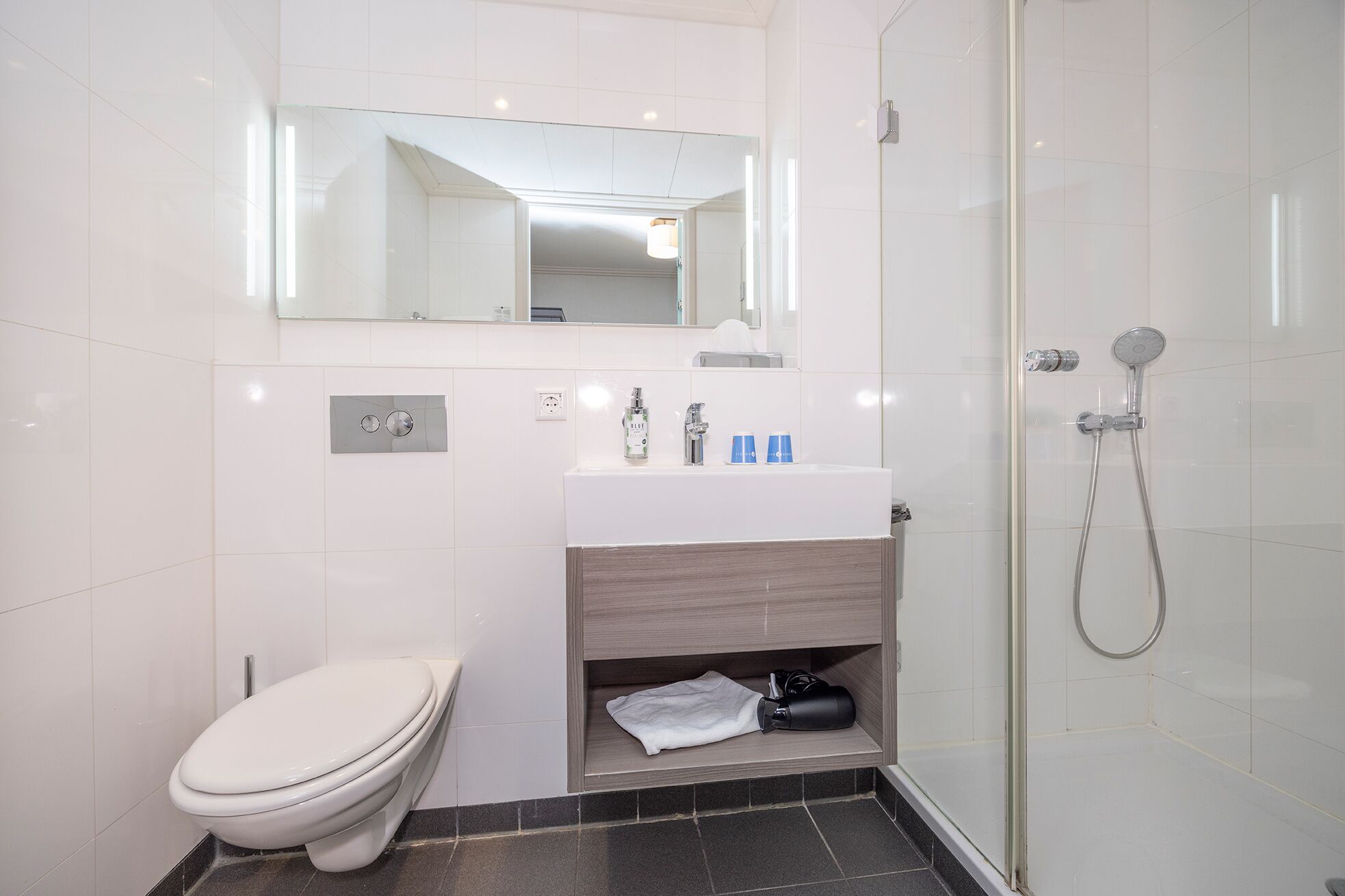 A modern bathroom with a white toilet, a sink with toiletries, a mirror, and a shower area.