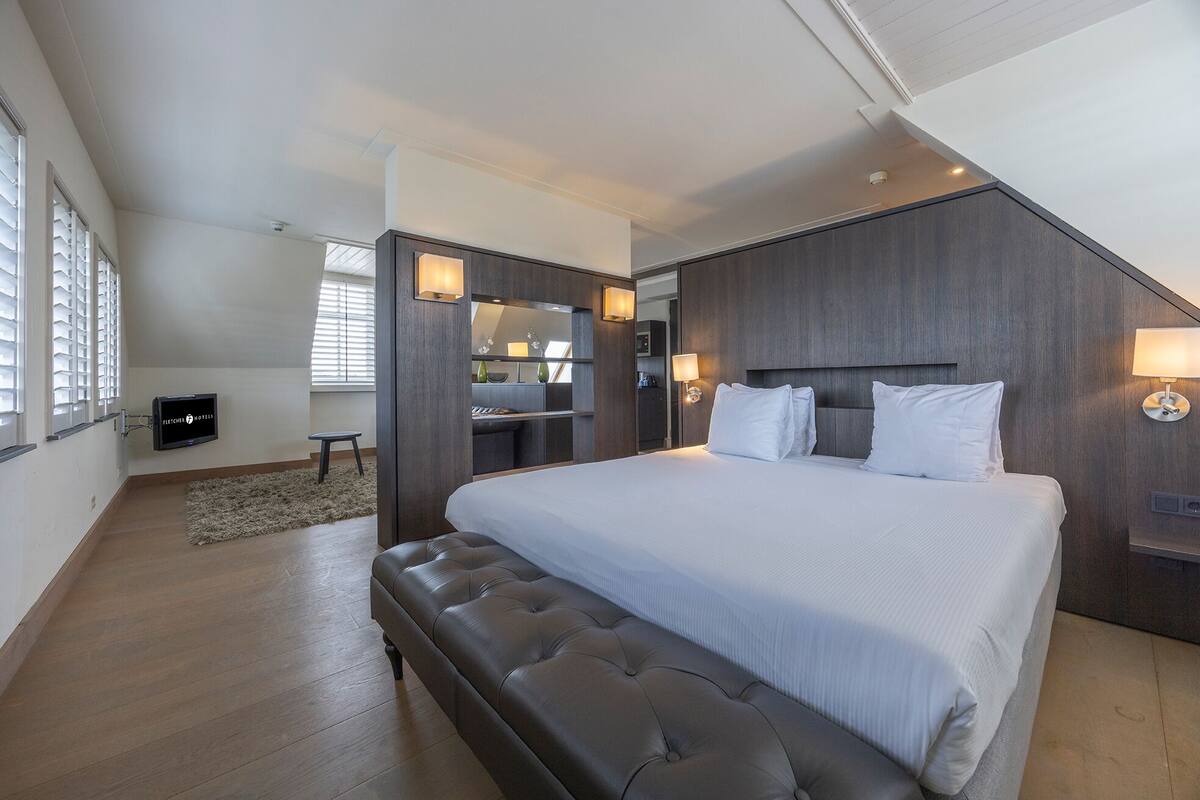 A modern bedroom with a large bed, a desk, and a seating area.