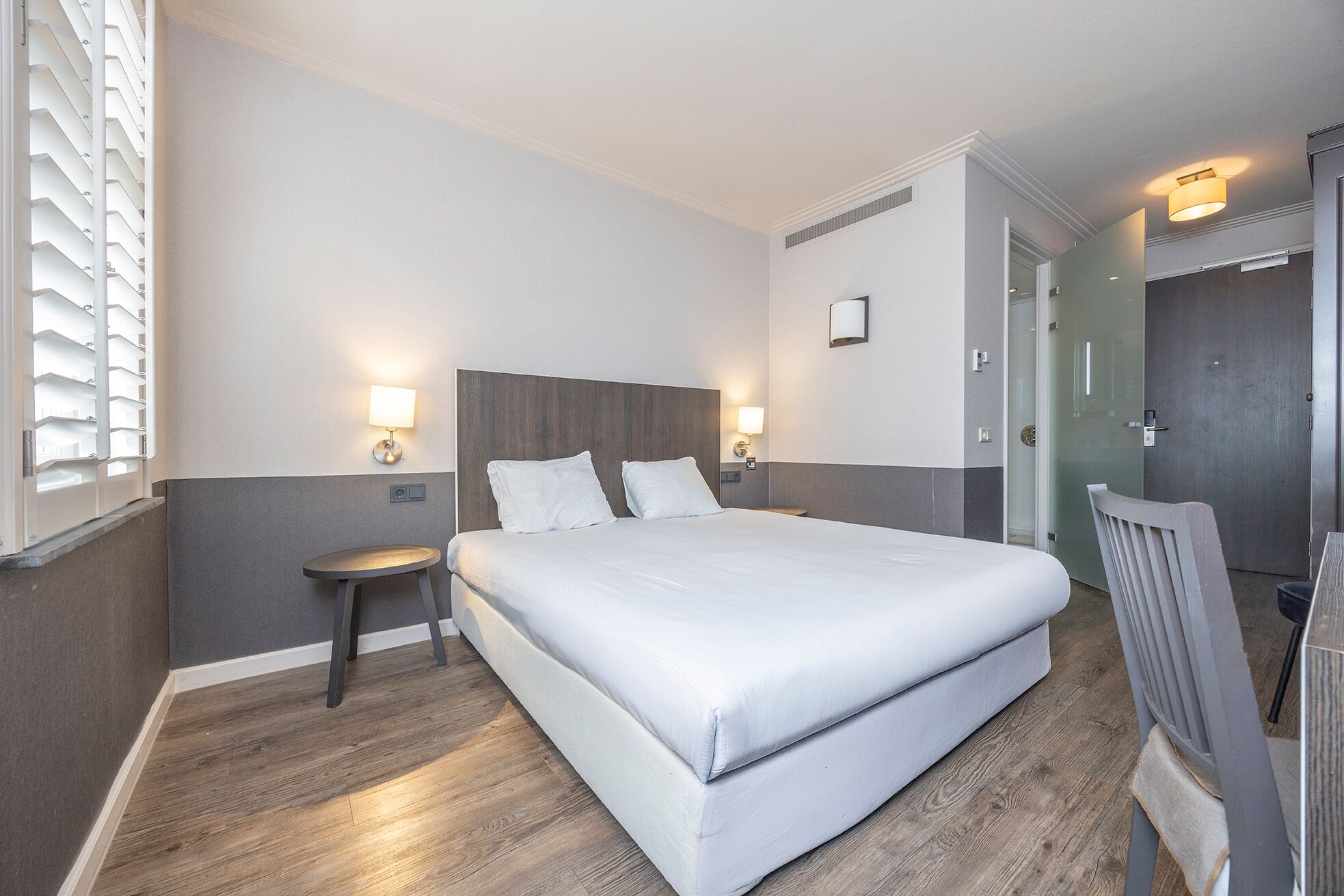 A hotel room with a large bed, two bedside tables, a chair, a desk, and a wardrobe.