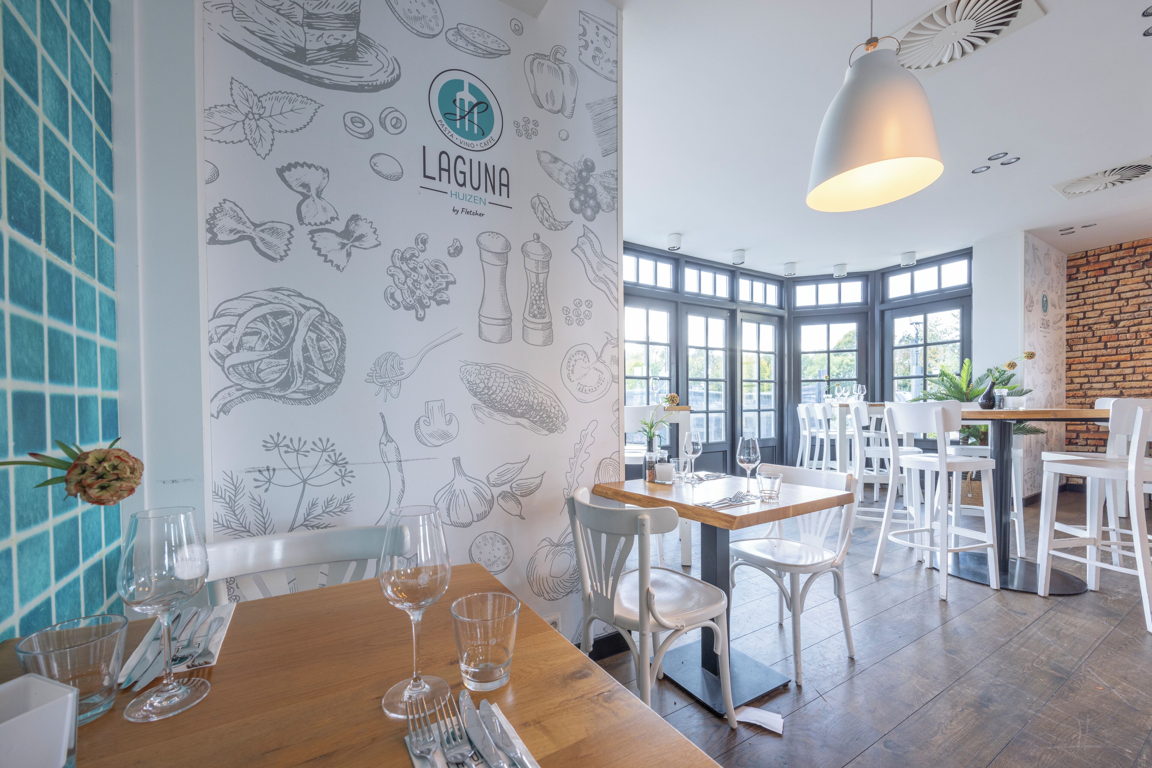 Een restaurantinterieur met een houten tafel, witte stoelen en een muur versierd met afbeeldingen van eten.
